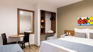 A hotel room with a bed, a desk, a chair, a small table, a wardrobe, and a painting on the wall.
