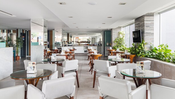 A modern hotel lobby with a central bar area, seating arrangements, and large windows providing natural light.