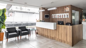 A modern reception area with a wooden reception desk, two black armchairs, a small table, and a large potted plant.