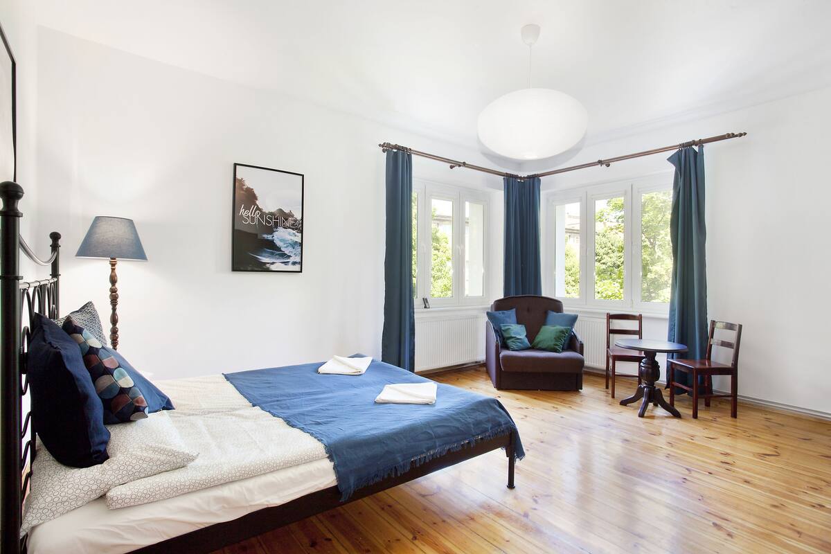 A bedroom with a bed, a chair, a table, and a window with curtains.