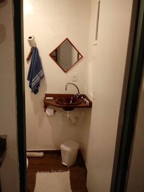 A small bathroom with a wooden sink, a mirror, a towel, and a trash bin. - Casinha Charmosa (Florianópolis)