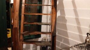 Een houten ladder in een keuken, met een fornuis en een groene deur op de achtergrond.