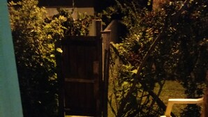 Een houten terras met een stoel en tafel, omgeven door weelderige begroeiing en een houten hek.