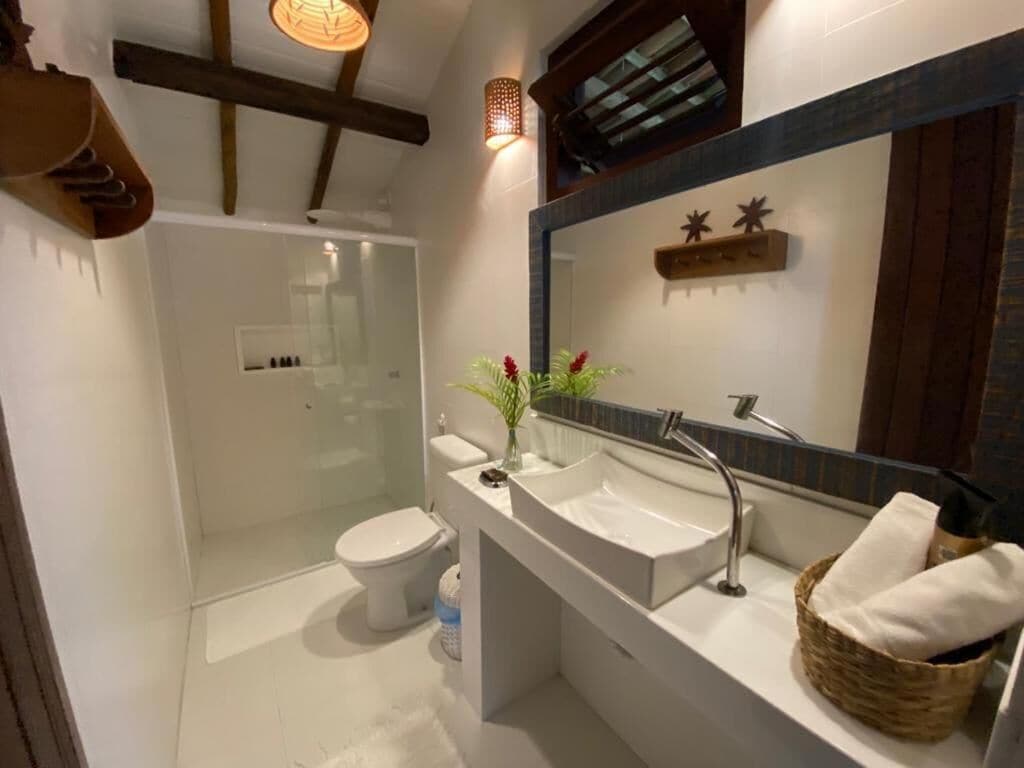 Un baño moderno con cabina de ducha de vidrio, inodoro blanco, tocador con un espejo grande y una cesta de toallas.