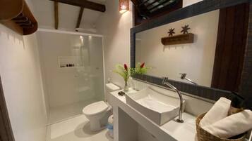 Un baño moderno con cabina de ducha de vidrio, inodoro blanco, tocador con un espejo grande y una cesta de toallas.