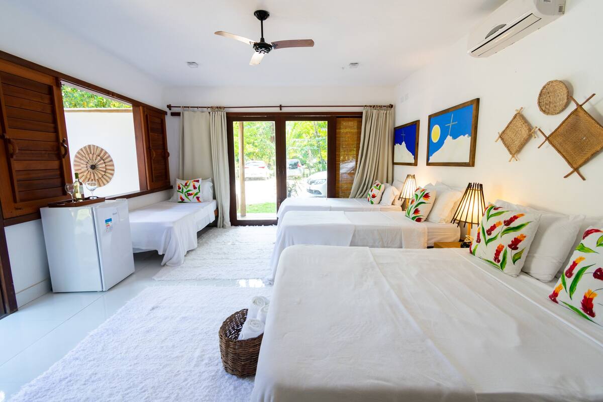 A hotel room with two beds, a ceiling fan, a refrigerator, and a view of the outdoors.