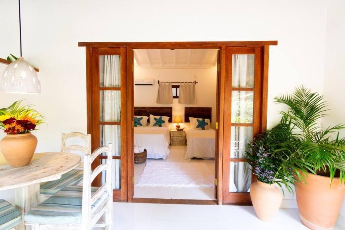 A room with a bed, a nightstand, a lamp, and two potted plants.