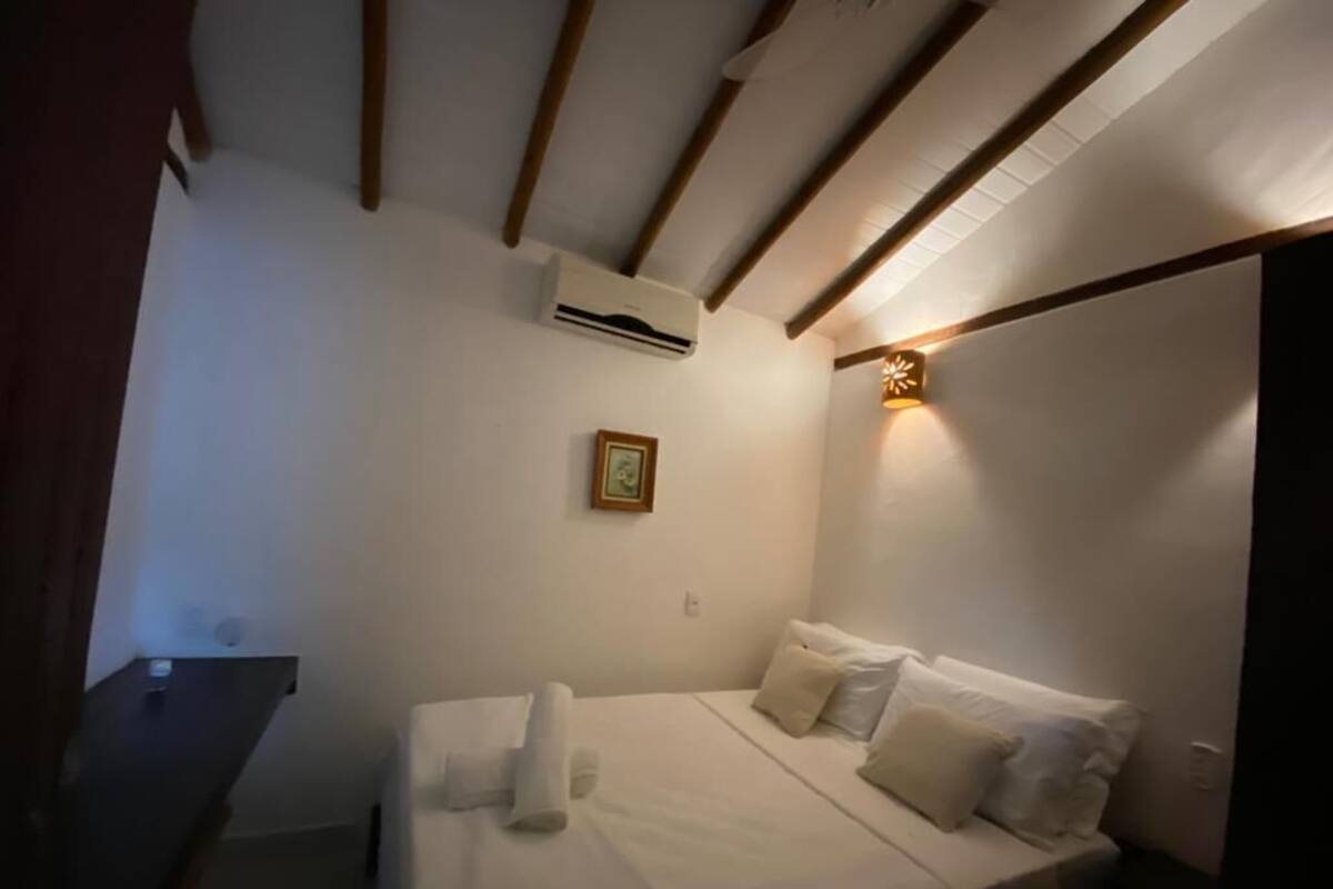 A bedroom with a bed, pillows, a bedside table, an air conditioning unit, and a wall-mounted light fixture.