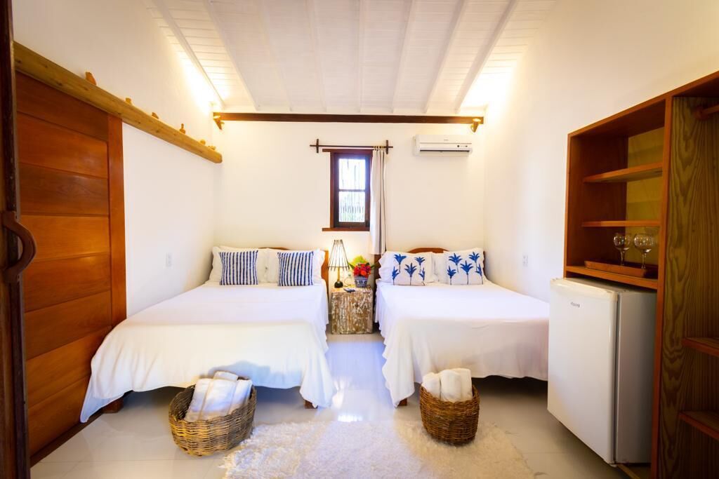 A bedroom with two beds, a wooden wardrobe, a small refrigerator, and a window with curtains.