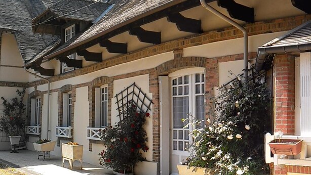 Un bâtiment traditionnel doté d’un toit en pente, de murs en briques et d’un balcon agrémenté de plantes en pot.