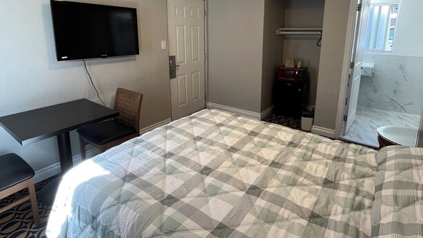 A hotel room with a bed, a desk, a chair, a television, a door, a microwave, and a bathroom with a mirror. - Griffith Park Motel - LA Hollywood Area (Glendale)