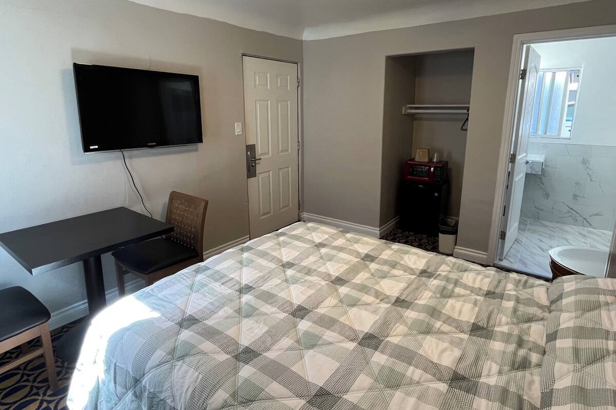 Une chambre d’hôtel équipée d’un lit, d’un bureau, d’une chaise, d’une télévision, d’une porte, d’un four à micro-ondes et d’une salle de bain avec un miroir.