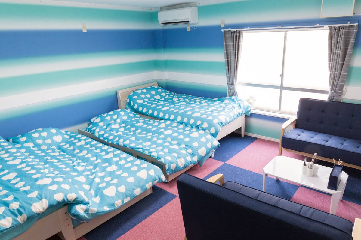 A room with two beds, a sofa, a small table, and a window with curtains.