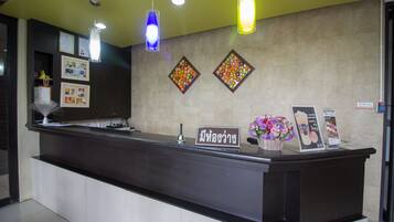 A reception desk with a dark counter, a sign with Thai script, framed pictures, and two decorative wall panels.