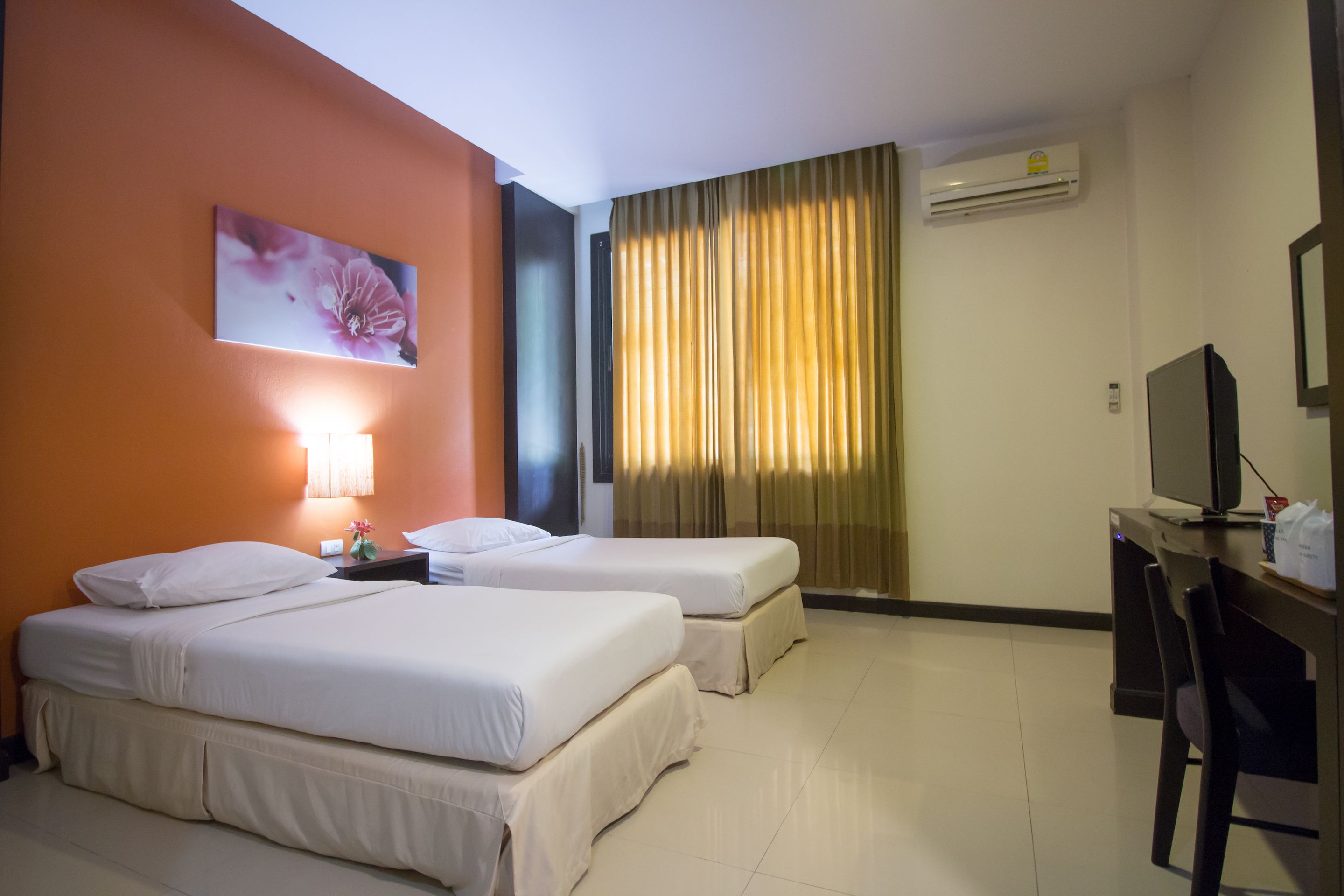 Habitación de hotel con dos camas, un escritorio, una silla, un equipo de aire acondicionado y una ventana con cortinas.