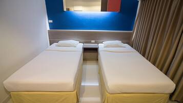 Quarto de hotel com duas camas de solteiro, uma mesinha, um espelho e uma janela com cortinas.