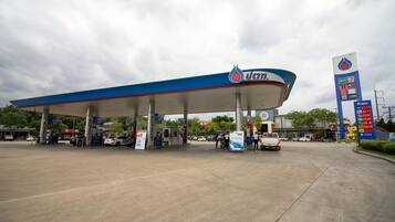 Una estación de servicio con toldo azul, varias bombas de combustible y un cartel grande que muestra los precios de los combustibles.