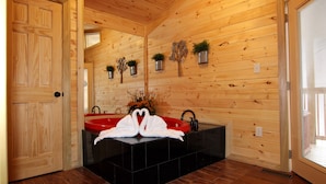 A wooden cabin bathroom with a red bathtub, black tiles, wooden walls, and potted plants.