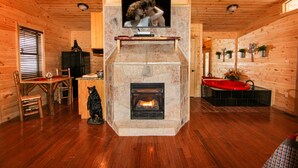 A cozy cabin interior with a stone fireplace, wooden walls, a television mounted above it, and a red bathtub.
