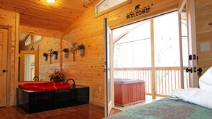 A wooden cabin interior with a red sink, a hot tub, and a quilted bedspread.