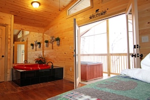 A wooden cabin interior with a red sink, a hot tub, and a quilted bedspread.