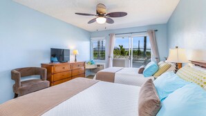 Une chambre d’hôtel avec deux lits, un ventilateur de plafond, une télévision, un bureau et une vue sur l’extérieur.