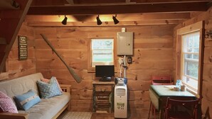 Ein gemütliches Blockhaus mit Holzvertäfelung, einer Couch, einem Tisch, einem Sessel, einem Fernseher und einer Heizung.