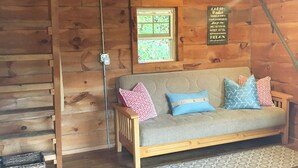 Ein Holzblockbau-Innenraum mit einer Couch, Kissen, einem Fenster und einem Schild an der Wand.