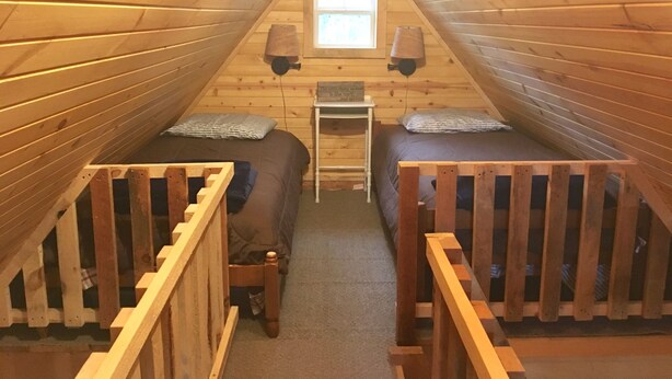 Une petite chambre mansardée avec deux lits superposés en bois, une petite table et une fenêtre.
