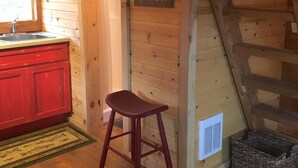 Ein Holzblockhaus-Interieur mit einer Küchenzeile, einem roten Hocker, einer Leiter und einem an der Wand befestigten Schild.