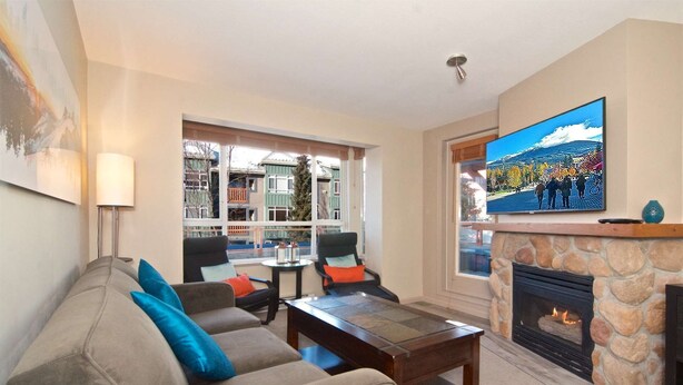 A living room with a sofa, chairs, a coffee table, a fireplace, a TV, and a window with a view of buildings.
