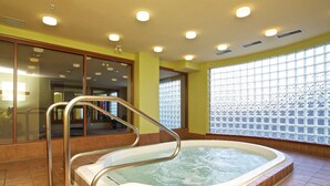 A hot tub in a room with yellow walls, large windows, and a metal railing.