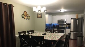 A dining area with a table, chairs, a chandelier, and a kitchen in the background.
