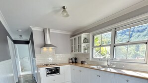 A kitchen with white cabinets, a stone tile floor, and a window with a view of greenery. - Hunter Valley - Romantic luxury spa cottage - awesome views  Cadair Cottage No 2 (Rosebrook)
