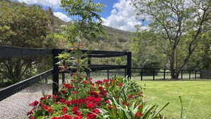 A garden with red flowers and a wooden pergola. - Hunter Valley - Romantic luxury spa cottage - awesome views  Cadair Cottage No 2 (Rosebrook)