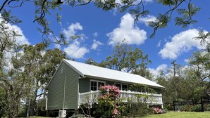 A two-story house with a white porch, surrounded by a well-maintained lawn and flowering plants. - Hunter Valley - Romantic luxury spa cottage - awesome views  Cadair Cottage No 2 (Rosebrook)