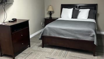 A hotel room with a bed, a desk, a chair, a lamp, and a television.