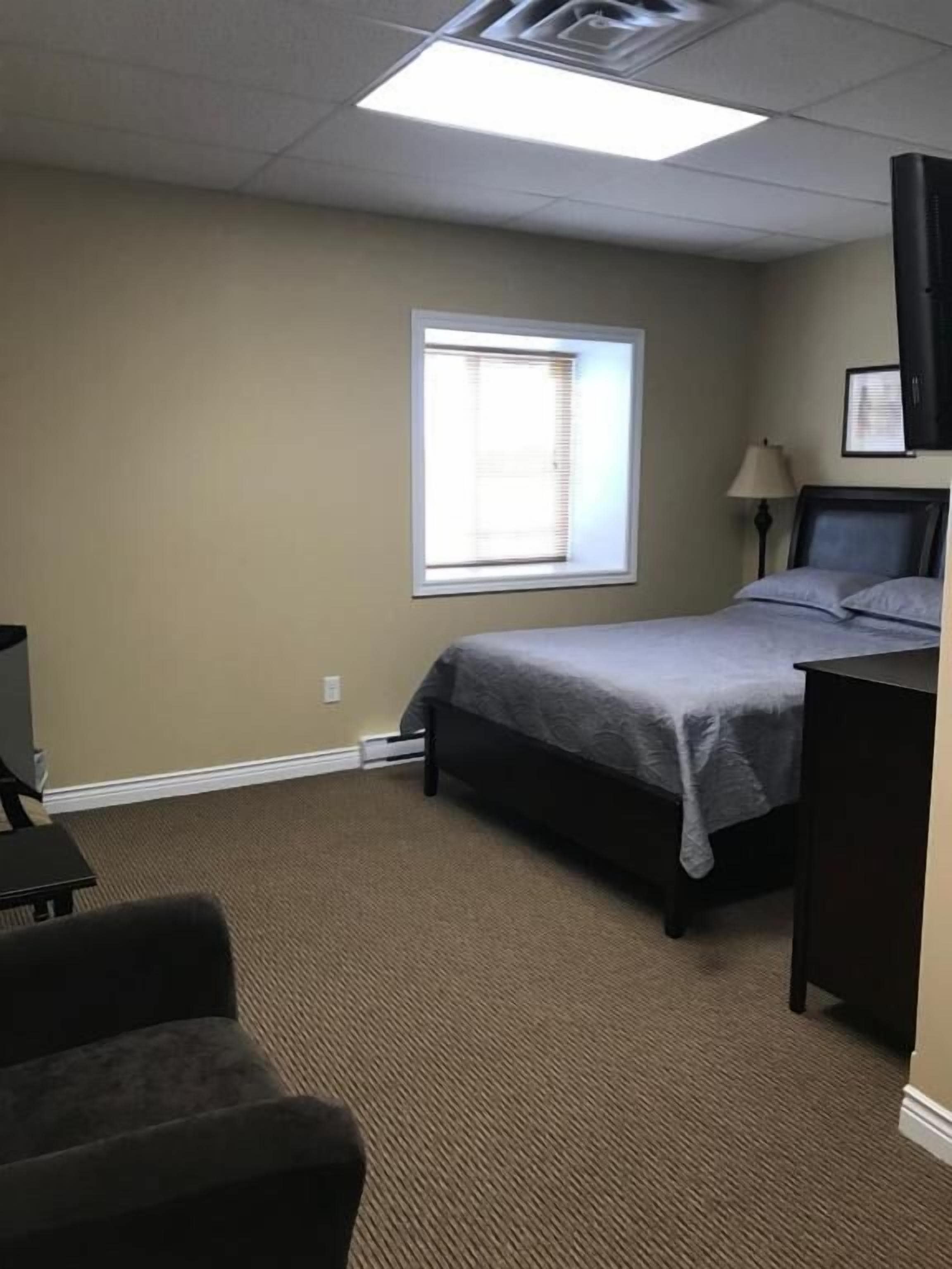 A hotel room with a bed, a desk, a chair, a window, and a ceiling vent.