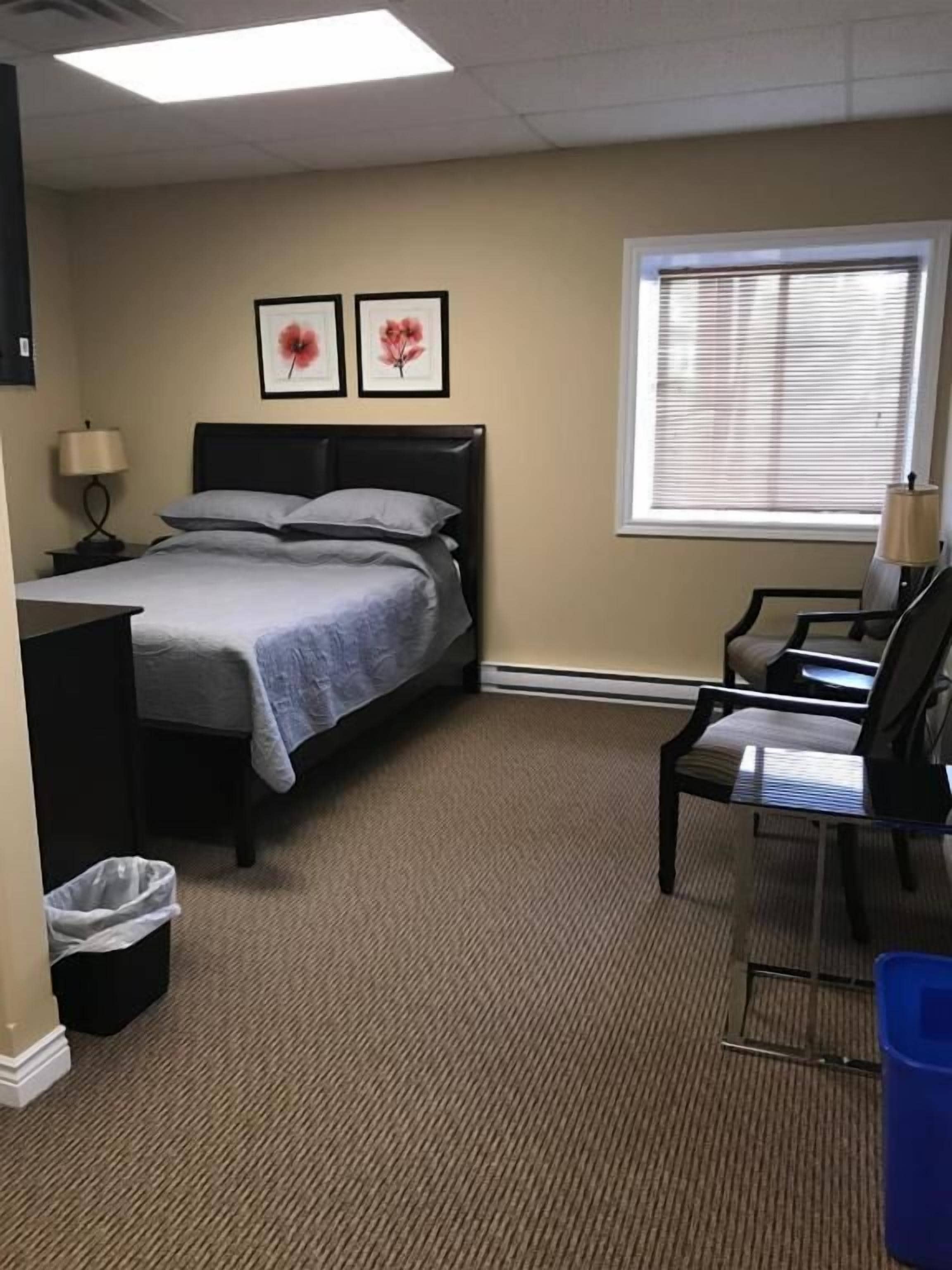 Une chambre d’hôtel équipée d’un lit, d’un bureau, d’une chaise, d’une fenêtre avec des stores et d’une poubelle.