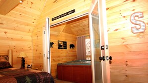 A cabin interior with a bed, a wooden wall with a bear silhouette, a sign reading "Welcome to our cabin," and a hot tub. - Gatlinburg Cabin Free Tickets, Heart Whirlpool, Hot Tub, King Bed, Fast Internet (Gatlinburg)