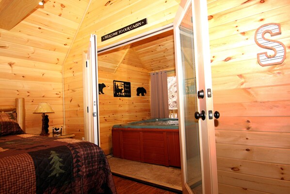 L’intérieur d’une cabane avec un lit, un mur en bois orné de la silhouette d’un ours, une pancarte sur laquelle on peut lire « Bienvenue dans notre cabane » et un bain à remous.