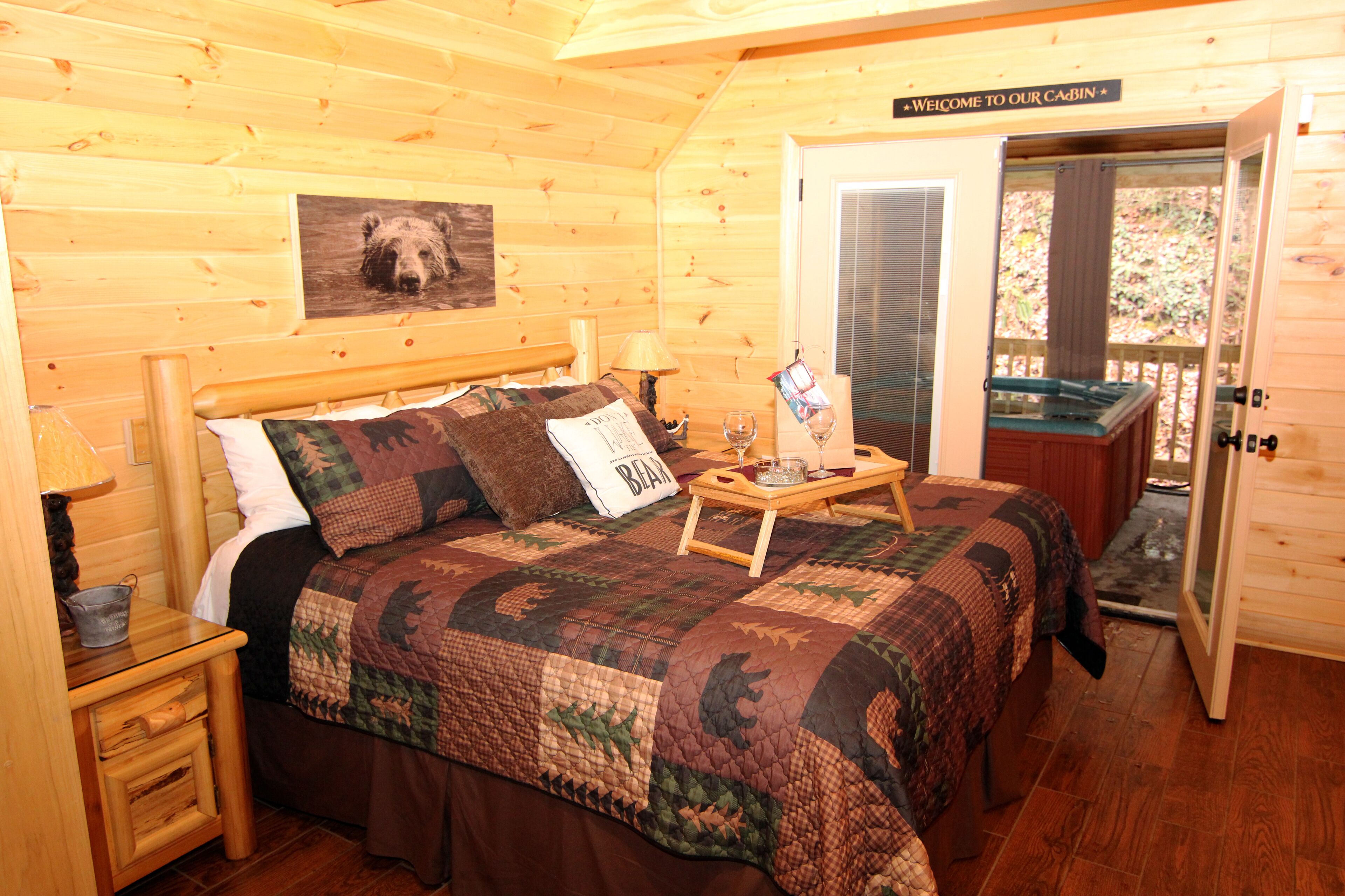 Une chambre de style cabane avec un lit, un panneau d’accueil, une table de chevet en bois et un verre d’eau sur un plateau.