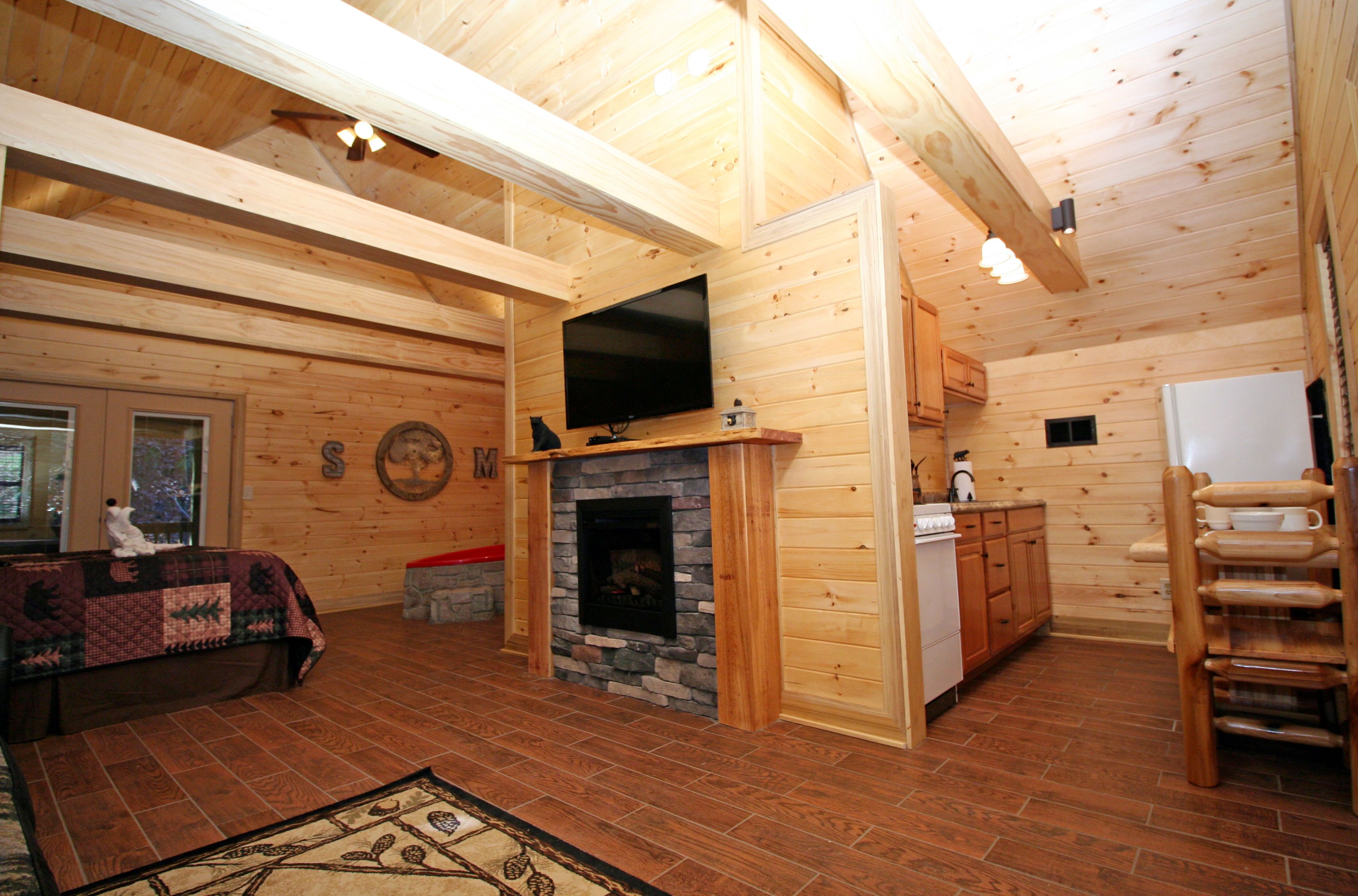 Ein gemütliches Blockhaus-Interieur mit Kamin aus Stein, Holzwänden, einem darüber angebrachten Fernseher und einem Essbereich mit Holzschränken.