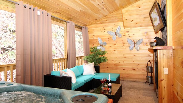 A cozy wooden cabin interior with a sofa, a small table with drinks, a fireplace, and a television mounted on the wall. - Gatlinburg Cabin Free Tickets, Heart Whirlpool, Hot Tub, King Bed, Fast Internet (Gatlinburg)