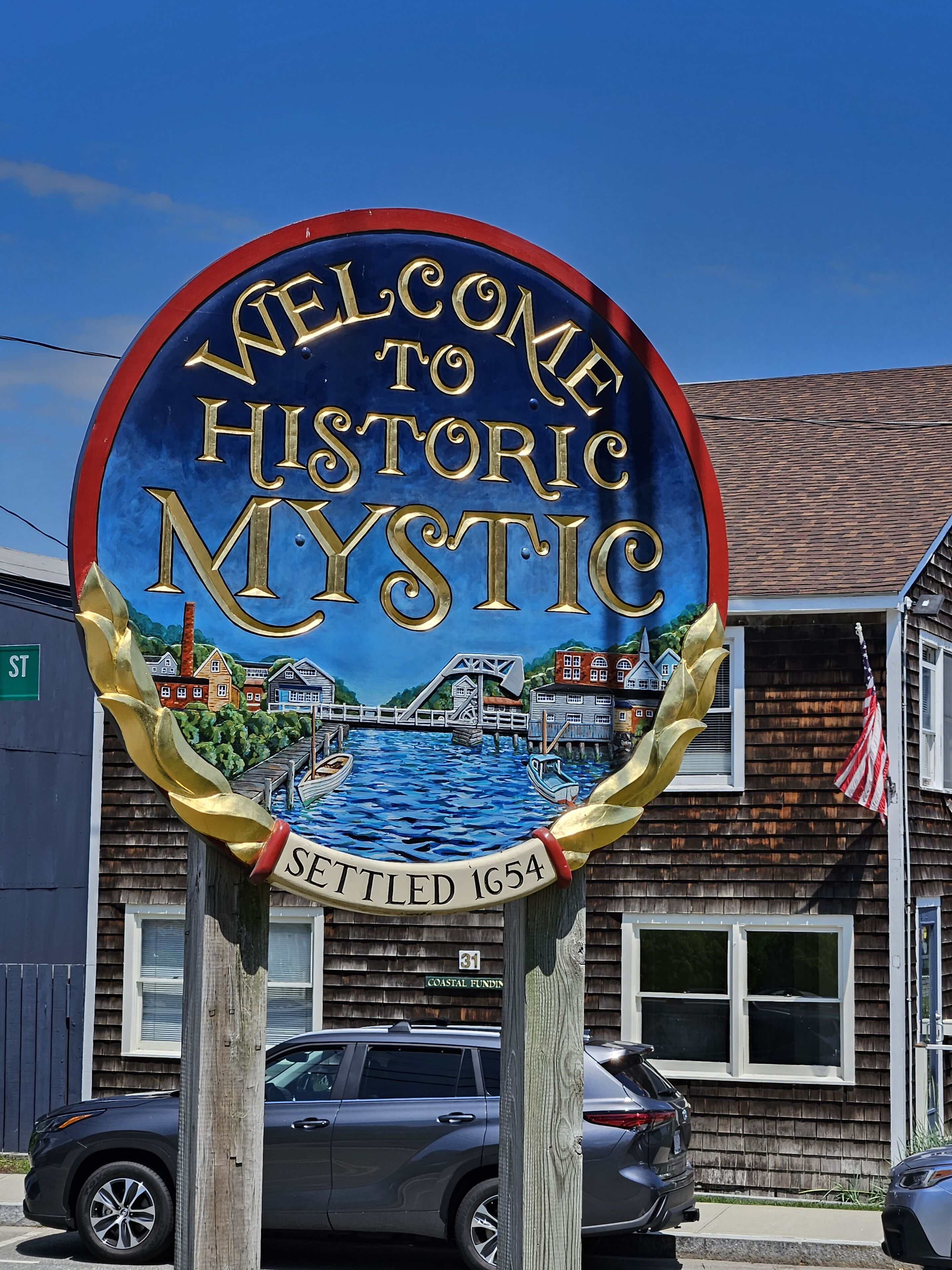 A welcome sign for Historic Mystic with a scenic illustration of a bridge and water, and the settlement year 1654.