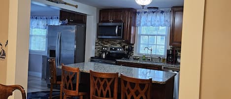 A kitchen with a central island, wooden chairs, and a dining table with chairs.