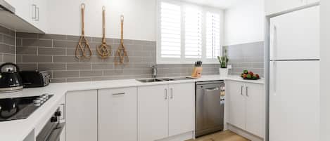 Una cocina moderna con armarios blancos, lavavajillas de acero inoxidable y estufa negra.