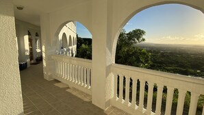 Varanda coberta com grades brancas e vista para uma paisagem verde.