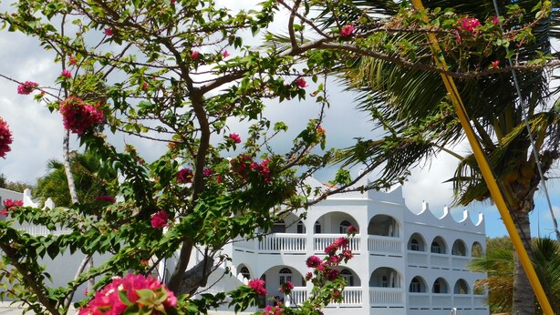 Um edifício branco com várias varandas e um jardim com flores cor-de-rosa.