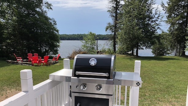 A portable grill on a deck with a lake view.